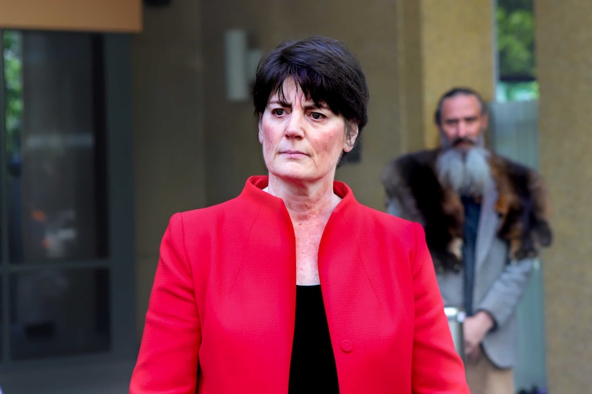 Fiona McLeod, with black hair, wearing a red jacket, stands outside the Coroner's Court.