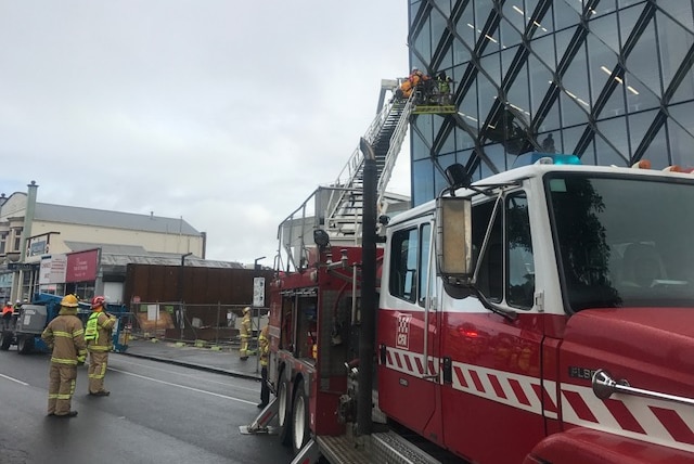 A fire truck extends a ladder to reach three men trapped in a cherry picker on a building site.