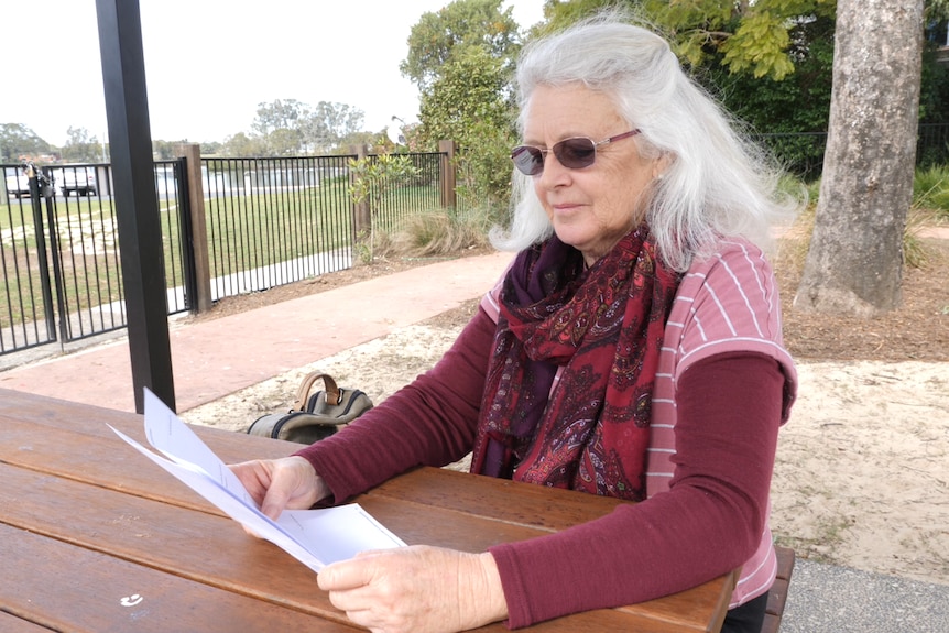 Woman in her sixties reading a letter sitting at a picnic table with sunglasses on.