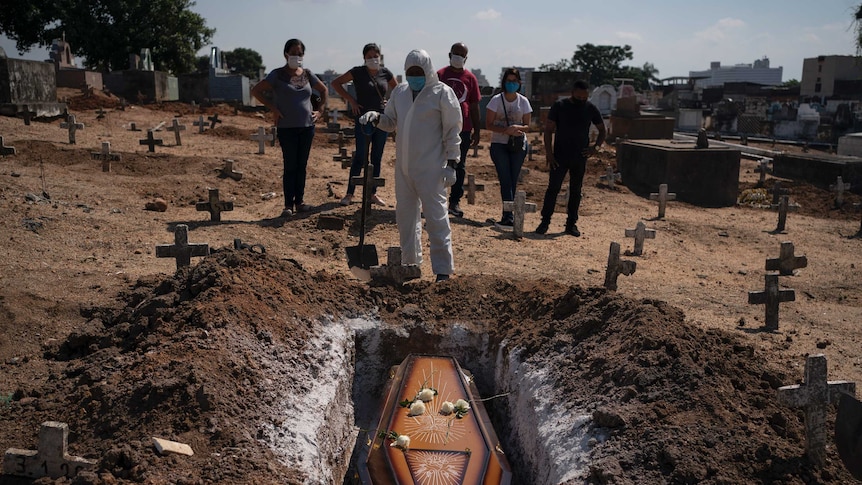 A cemetery worker stands before the coffin of a COVID-19 victim.