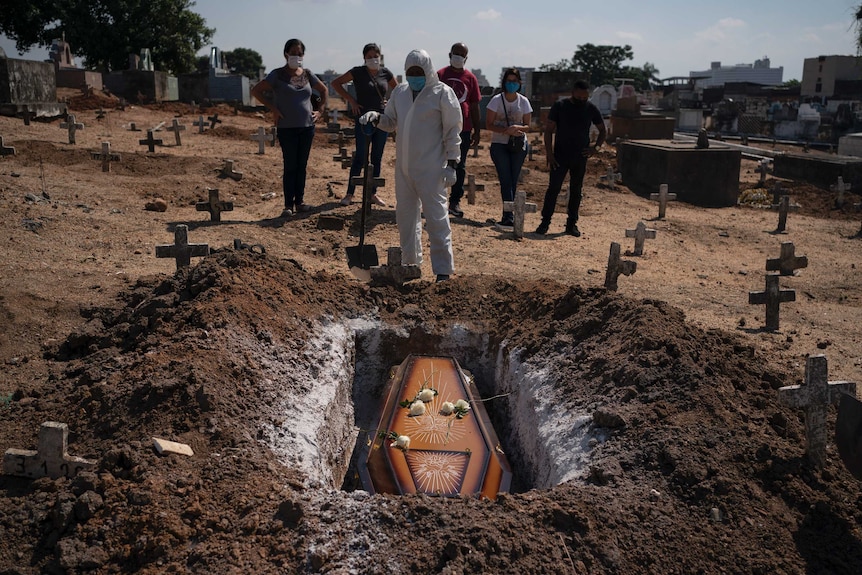 A cemetery worker stands before the coffin of a COVID-19 victim.