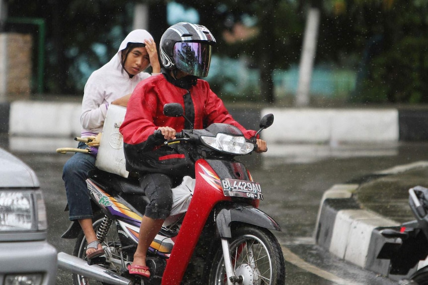 An Acehnese woman rides on the back side of a motorcycle