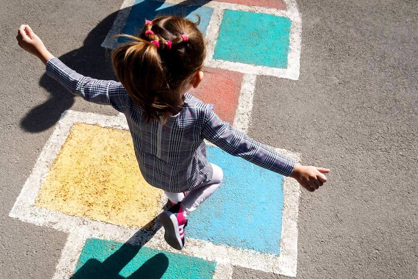 A young primary school girl balancing on a hopscotch square. Her arms are outstretched as she balances on one leg.
