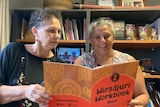 Sisters Lynette and Diane each hold a corner of a Wiradjuri language workbook, reading its contents.
