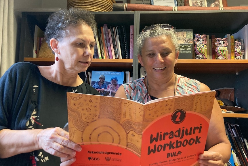 Sisters Lynette and Diane each hold a corner of a Wiradjuri language workbook, reading its contents.