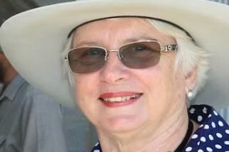 A woman with sunglasses with a white hat and blue polka dot shirt 