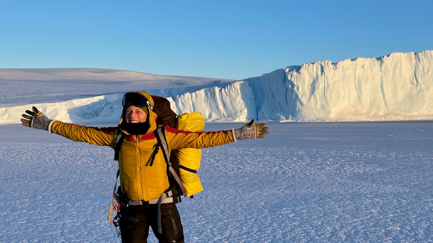 Gemma Woldendorp holds out her arms while wearing a yellow jacket at Mawson research station in Antarctica