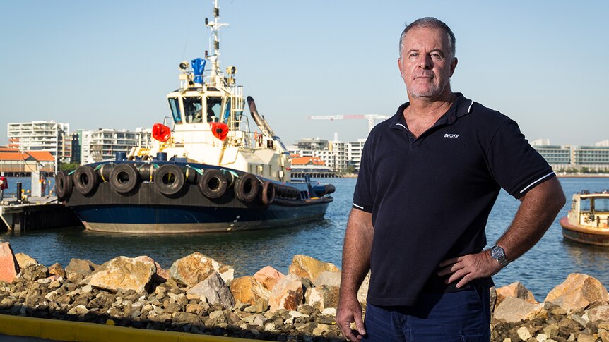 Geoff Ball stands on a dock with a tug in the background.