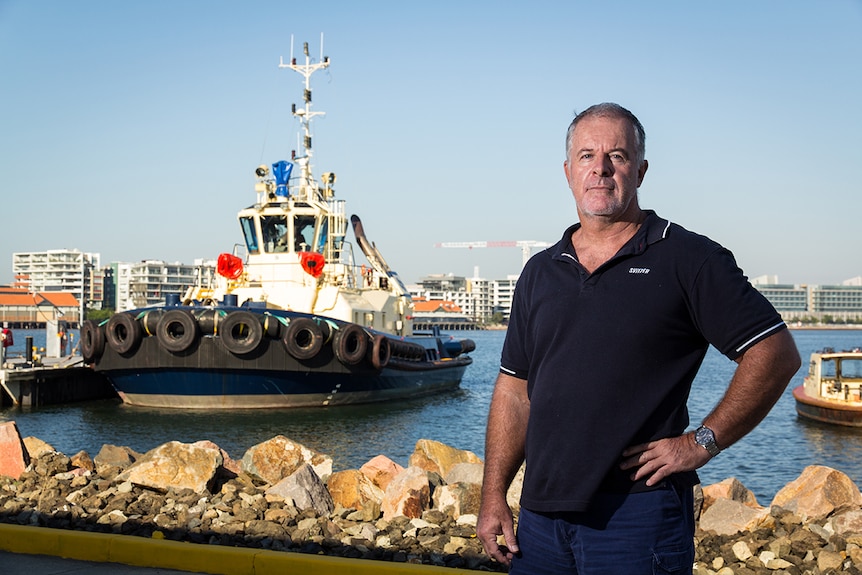 Geoff Ball stands on a dock with a tug in the background.