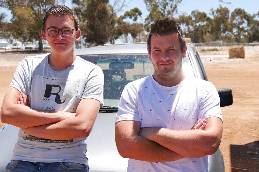 Two men in tee shirts lean against a car