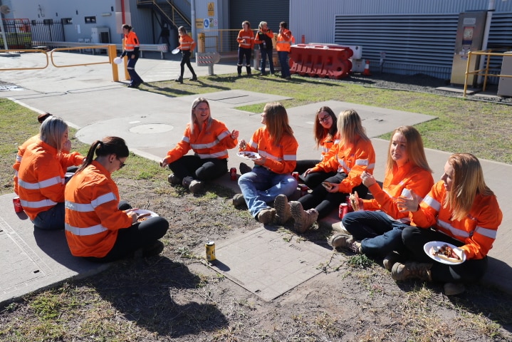 Group of women wearing hi-vis sit together, eating lunch