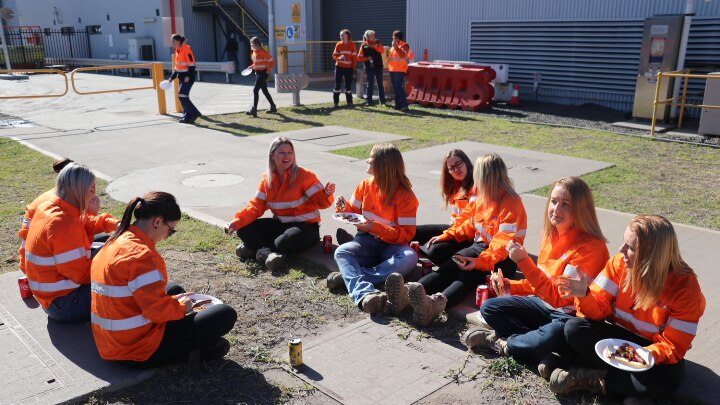 Group of women wearing hi-vis sit together, eating lunch