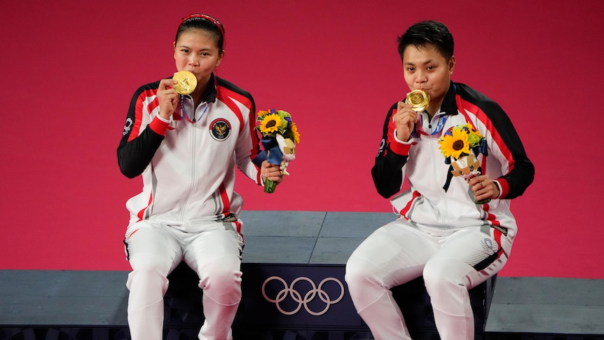 Two women sit smiling with Olympic gold medals