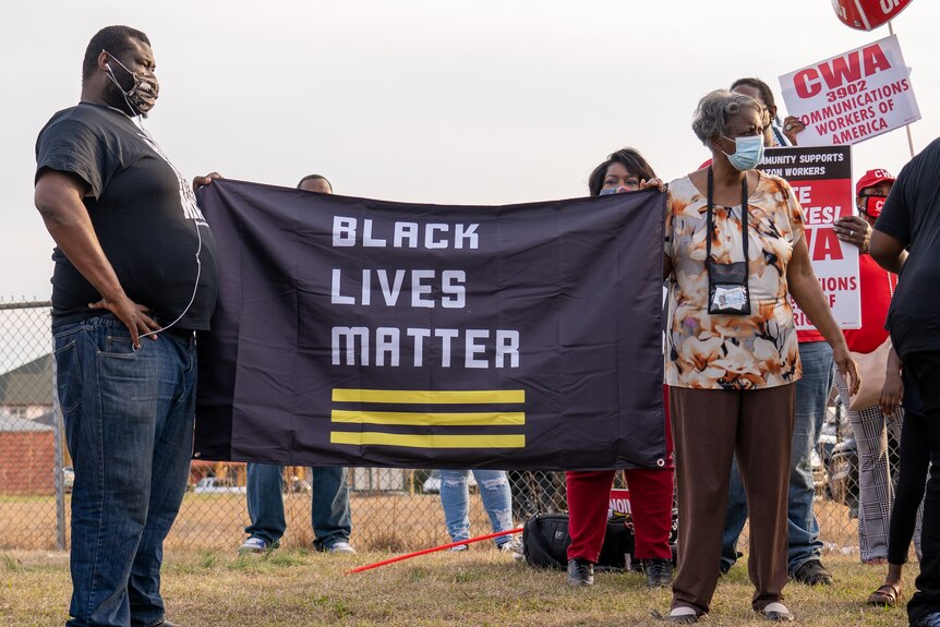 Two people hold up a banner reading "Black Lives Matter" among pro-union signs