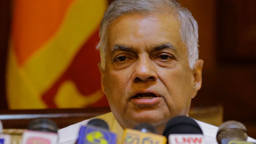 Sri Lankan Prime Minister Ranil Wickremesinghe speaks in front of a row of microphones with the Sri Lankan flag behind him