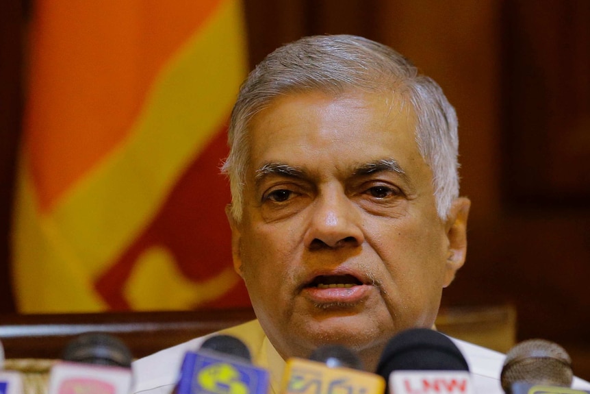 Sri Lankan Prime Minister Ranil Wickremesinghe speaks in front of a row of microphones with the Sri Lankan flag behind him