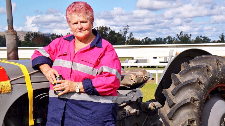 Sharon Way stands in a high-visibility pink shirt with her vintage tractor.