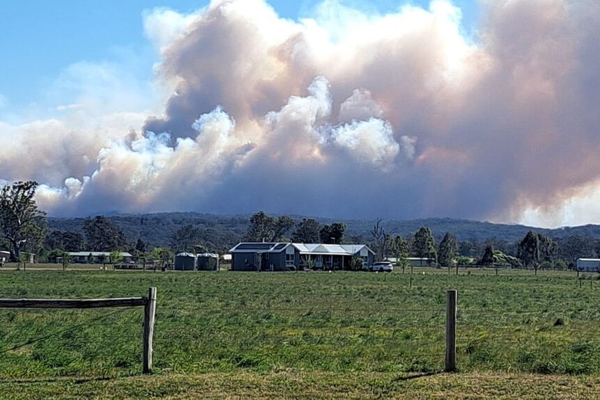 A house on a semi-rural block with a bushfire burning in the background.