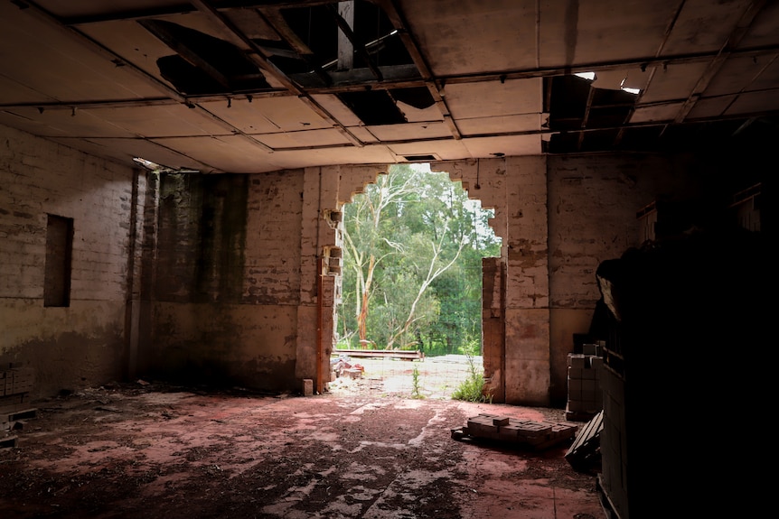 A dilapidated brick room with an archway through to a garden and bushland