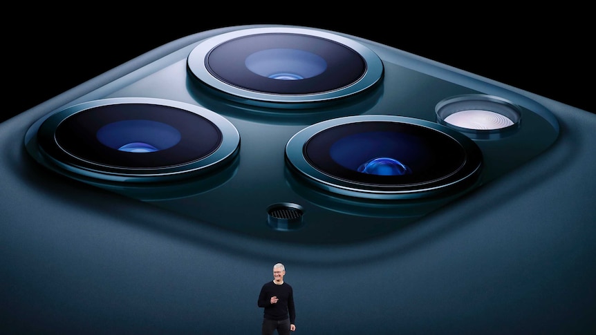 Tim Cook on stage in front of picture of iPhone 11 Pro cameras