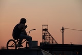 A young man on a bike with the Mount Isa Mine in the background