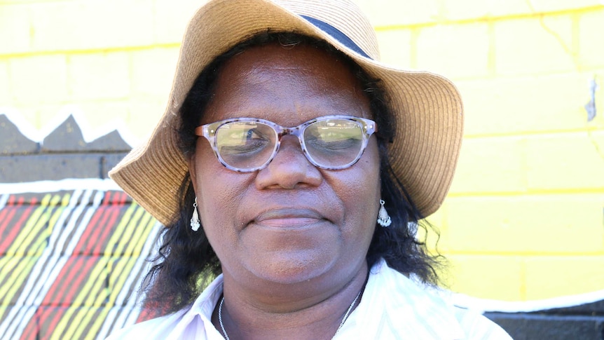 Anita Painter wears a white shirt, sunhat and purple-rimmed glasses and looks into the camera