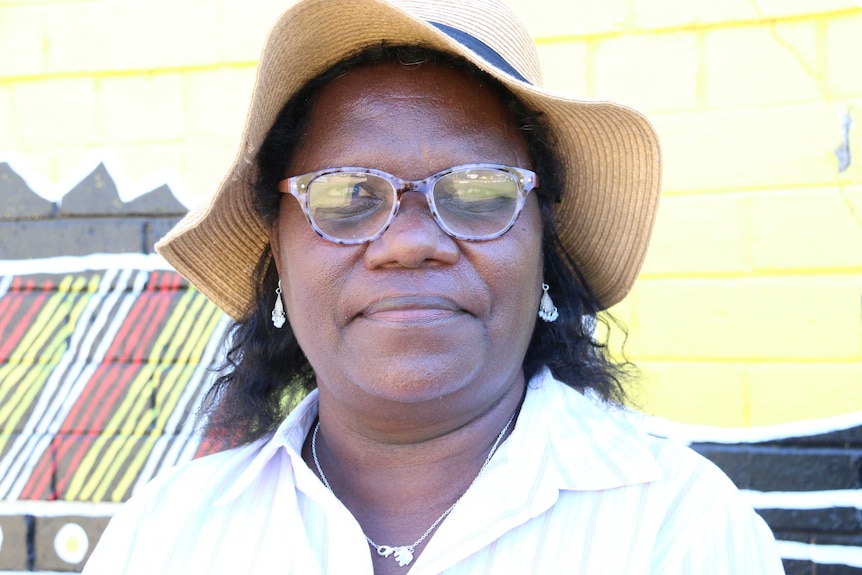 Anita Painter wears a white shirt, sunhat and purple-rimmed glasses and looks into the camera