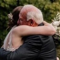 side view of woman in wedding gown holding bouquet of flowers embraces an older man with bald head and grey hair above ears