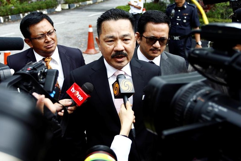 Rusdi Kirana is surrounded by microphones and television camera, flanked by two other men in suits