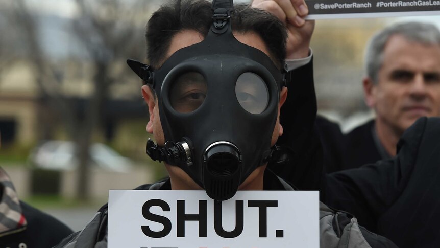 Porter ranch resident with a gas mask holds a sign saying "Shut it all down".