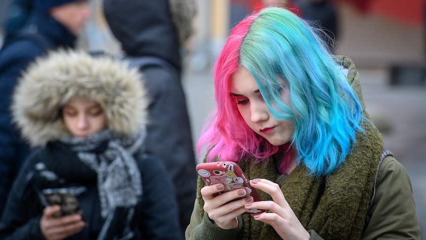 Young women look at their mobile phones on a street 