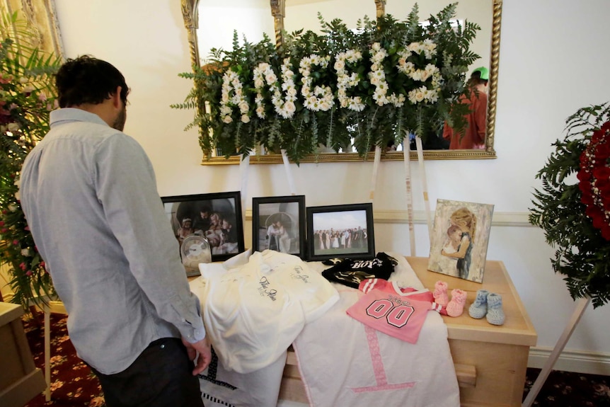 A man looks over a coffin that is decorated with pictures and clothes