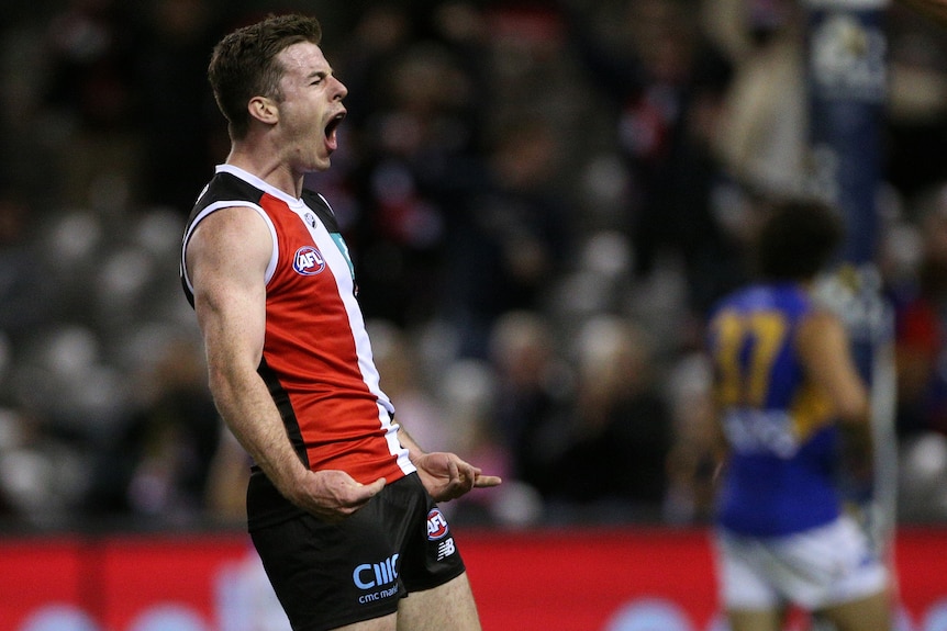 A St Kilda AFL player pumps his fists and screams out as he celebrates a goal.
