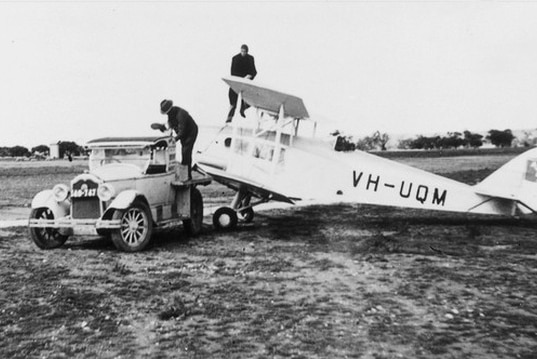 Black and white photo of two men, a vintage car and a single engine plane circa 1928.
