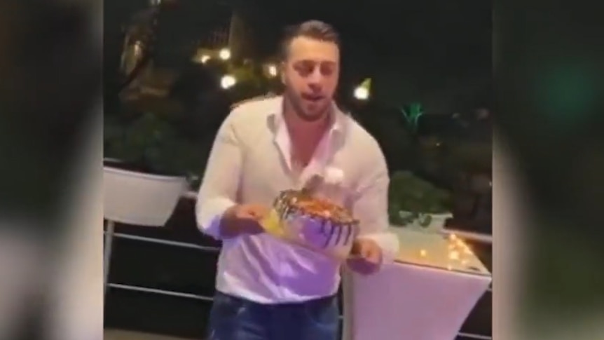 A young man in a white shirt cradles what appears to be a birthday cake with two lit candles