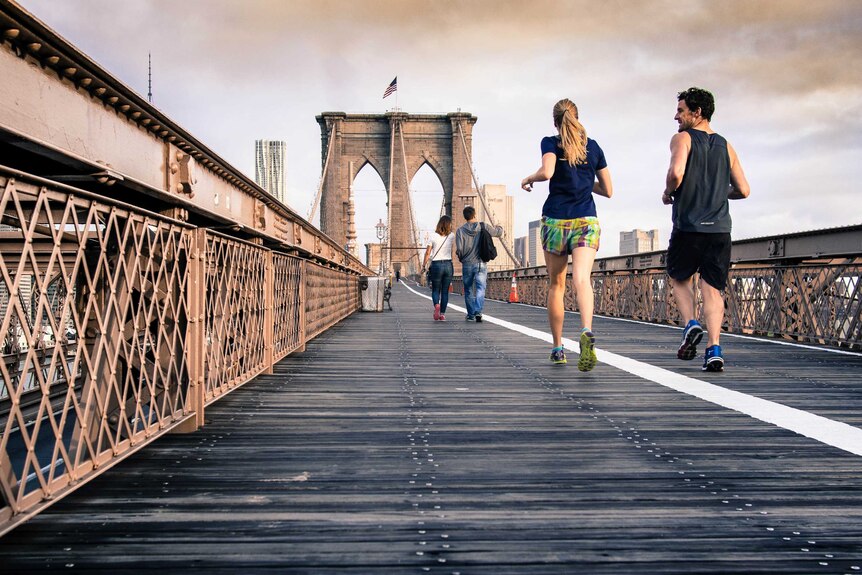 A man and a woman jog across a bridge.