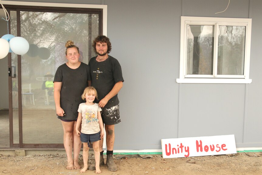 Nicole and Toby and their daughter Layla stand outside the makeshift home volunteers have built for them.
