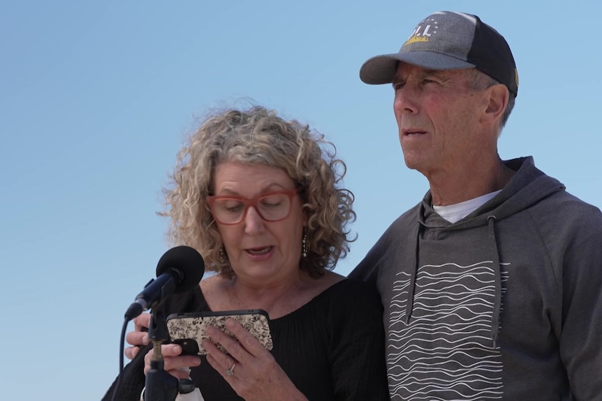 The couple stand together as Debra speaks into a microphone