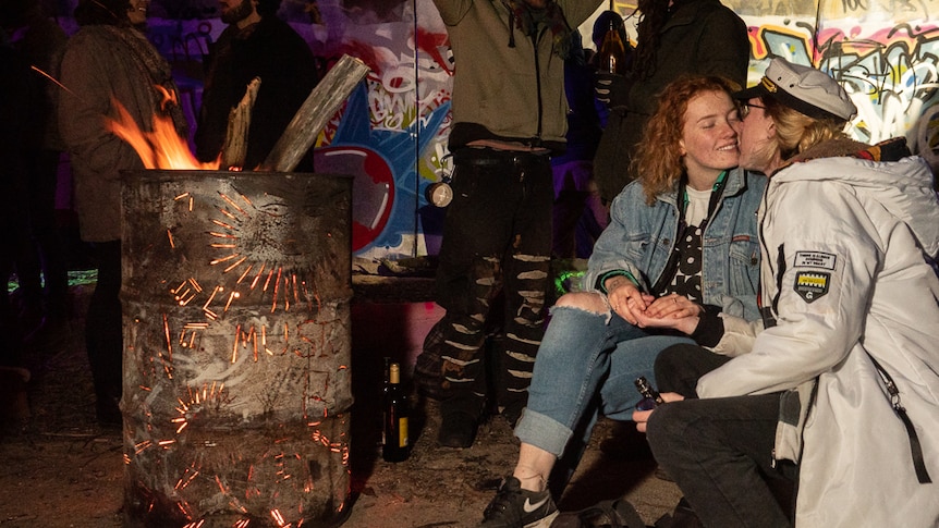 A young couple kiss beside a flaming drum