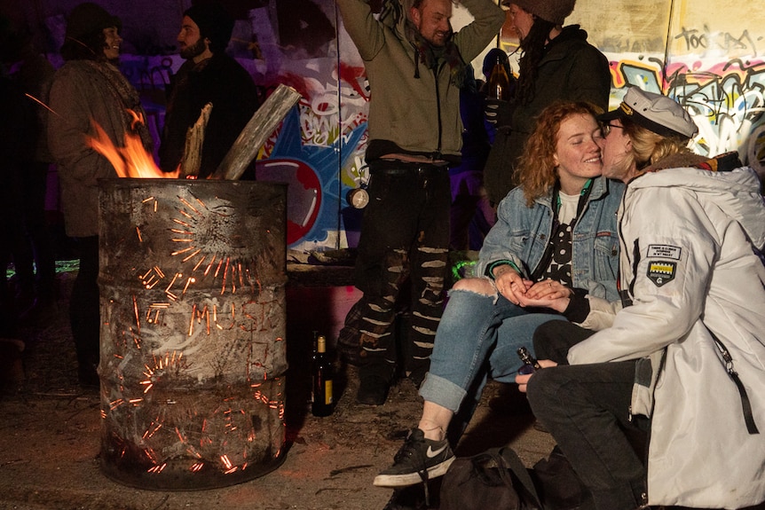 A young couple kiss beside a flaming drum