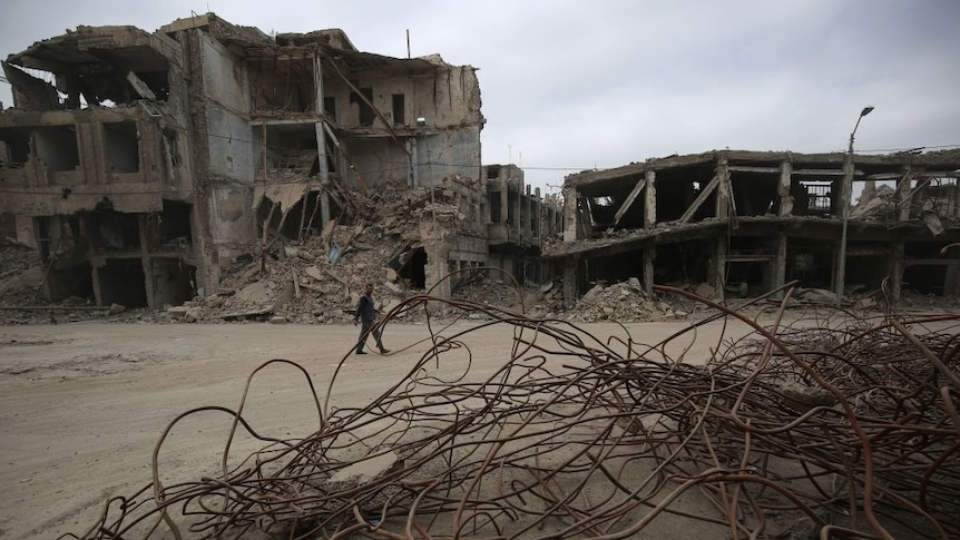 Man walks in residential area in Mosul after its liberation from the Islamic State group. Big destroyed buildings in background.