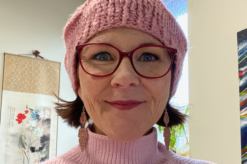 A close up of Shaz Attree pictured wearing a pink beanie, glasses and pink turtleneck
