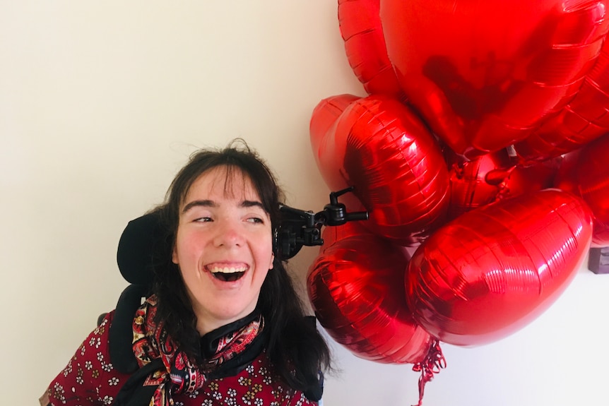 Kim Hopton  smiling sitting in a wheelchair with red balloons.