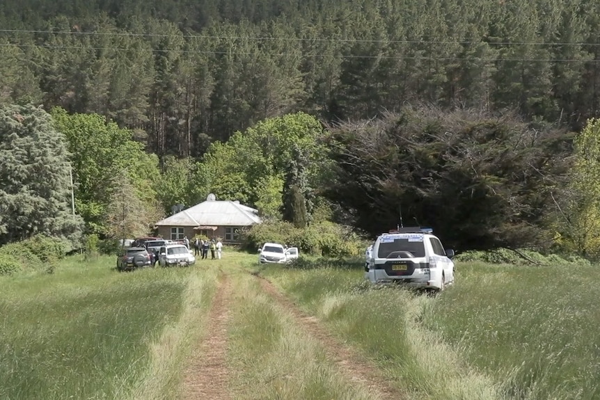 A rural house surrounded by police cars and long grass.