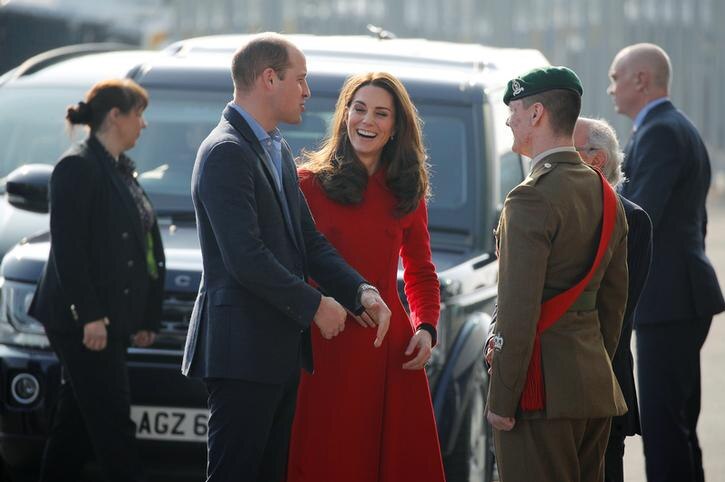 William, left, wears navy suit and blue shit. Kate, right, wears red coat and grins as the pair stand next to man in khaki.