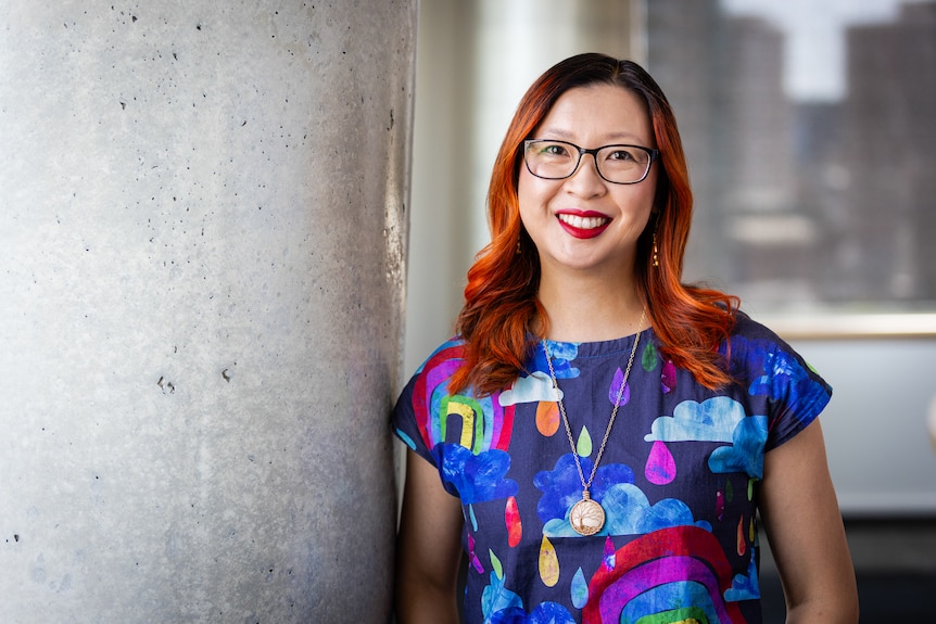 Dr Amanda White in a colourful patterend top with rainbow prints, glasses and dyed orange hair