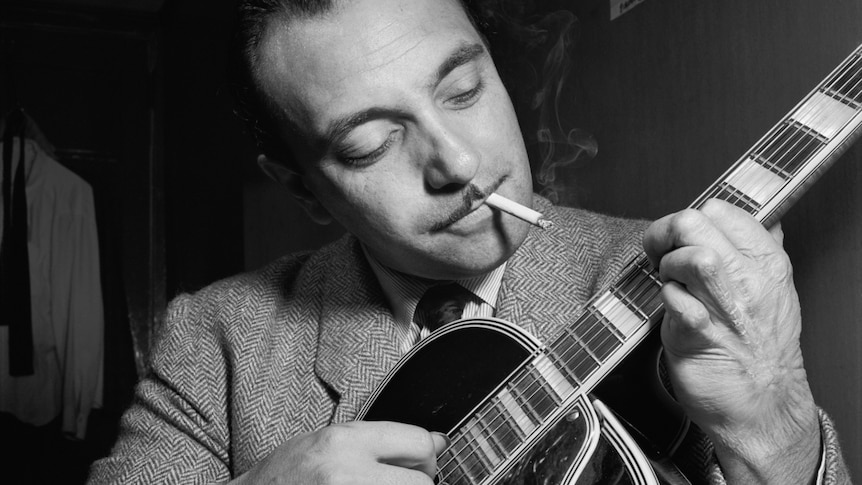 A monochrome shot of Django Reinhardt performing on his guitar while also smoking a cigarette