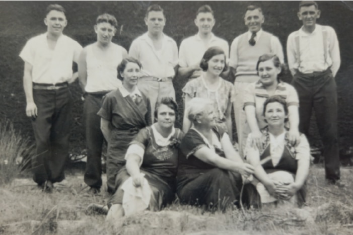 A black and white photo of six men standing, three women kneeling and three sitting, all smiling.