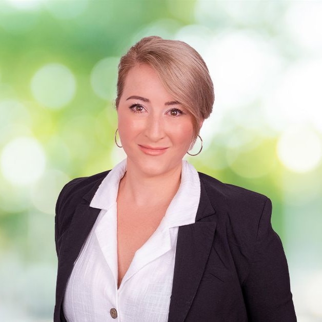 Woman with blonde hair in front of trees, gently smiling