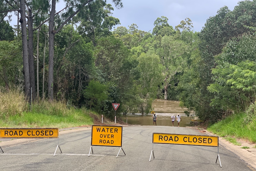 Roads closed signs in front of flood waters.